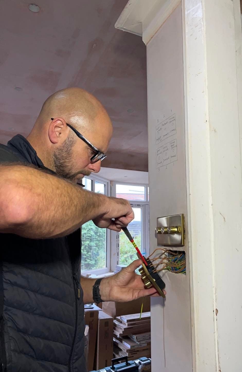 MW Electrical wiring a brass dimmer switch on site, working from a marked-up circuit plan