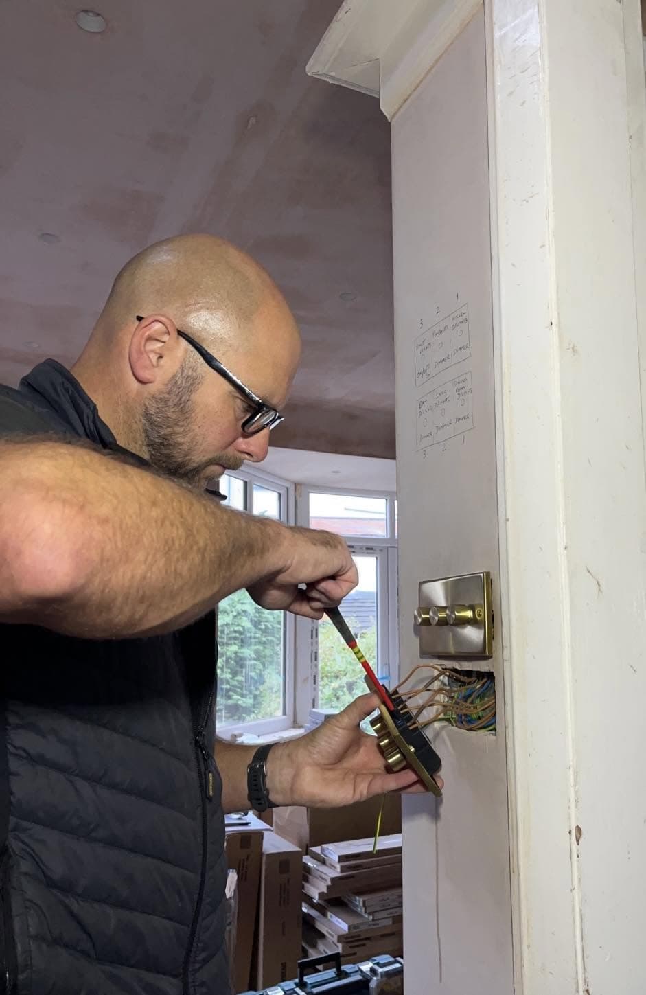 MW Electrical wiring a brass dimmer switch on site, working from a marked-up circuit plan