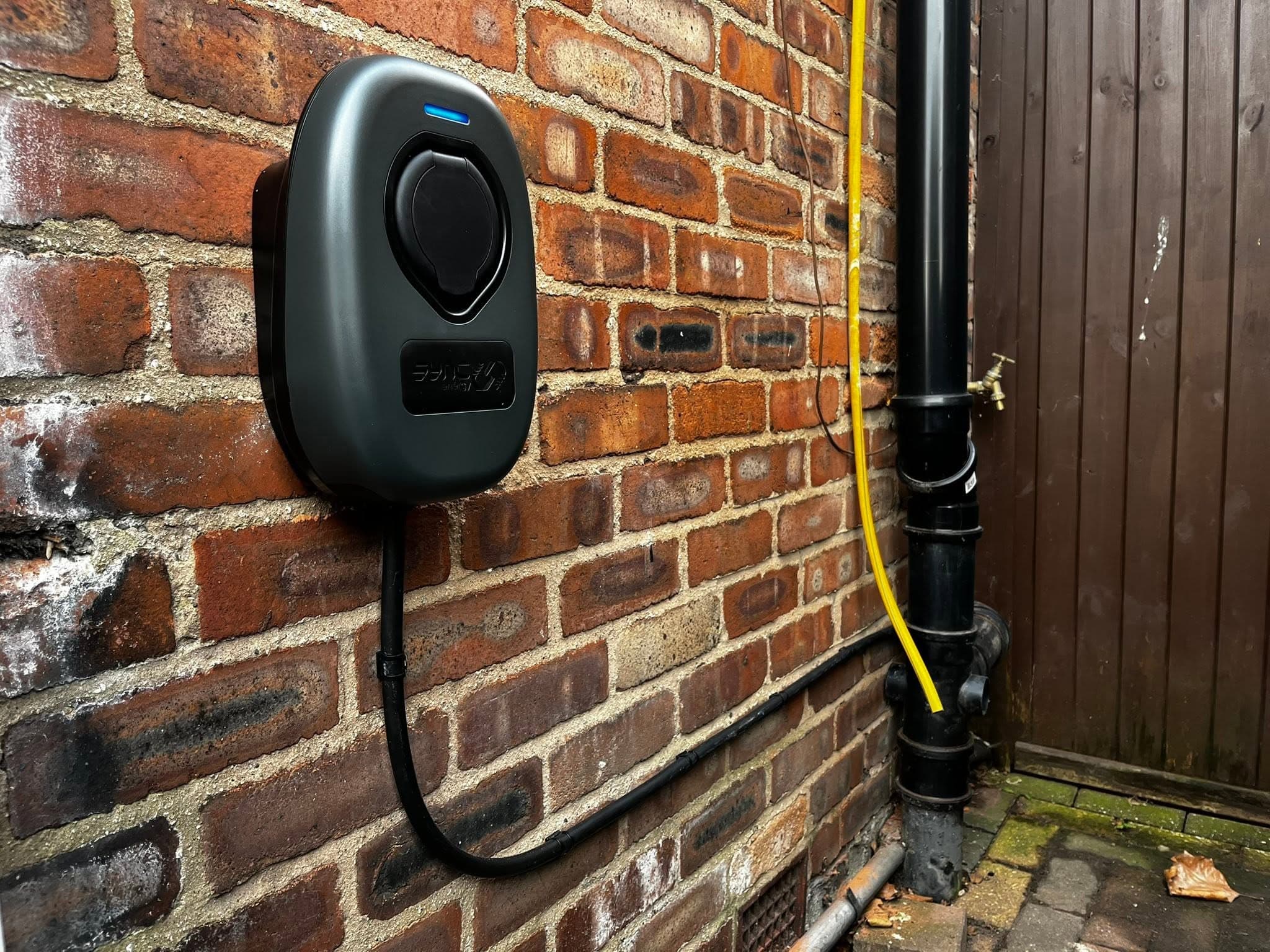Smart EV charger installed on a brick wall with neatly clipped cabling to the downpipe