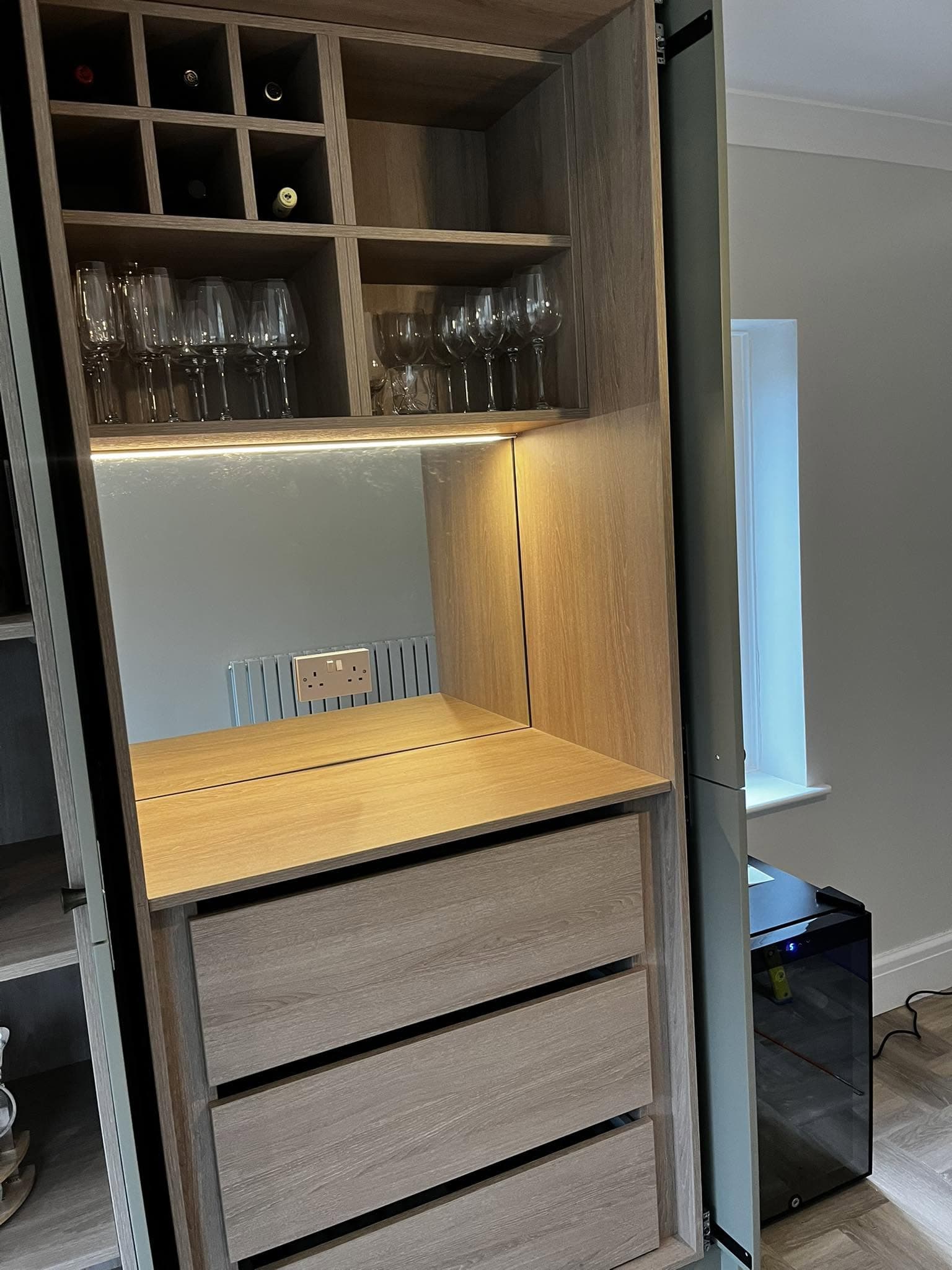 Built-in bar and wine unit with warm under-shelf LED lighting and a fitted socket