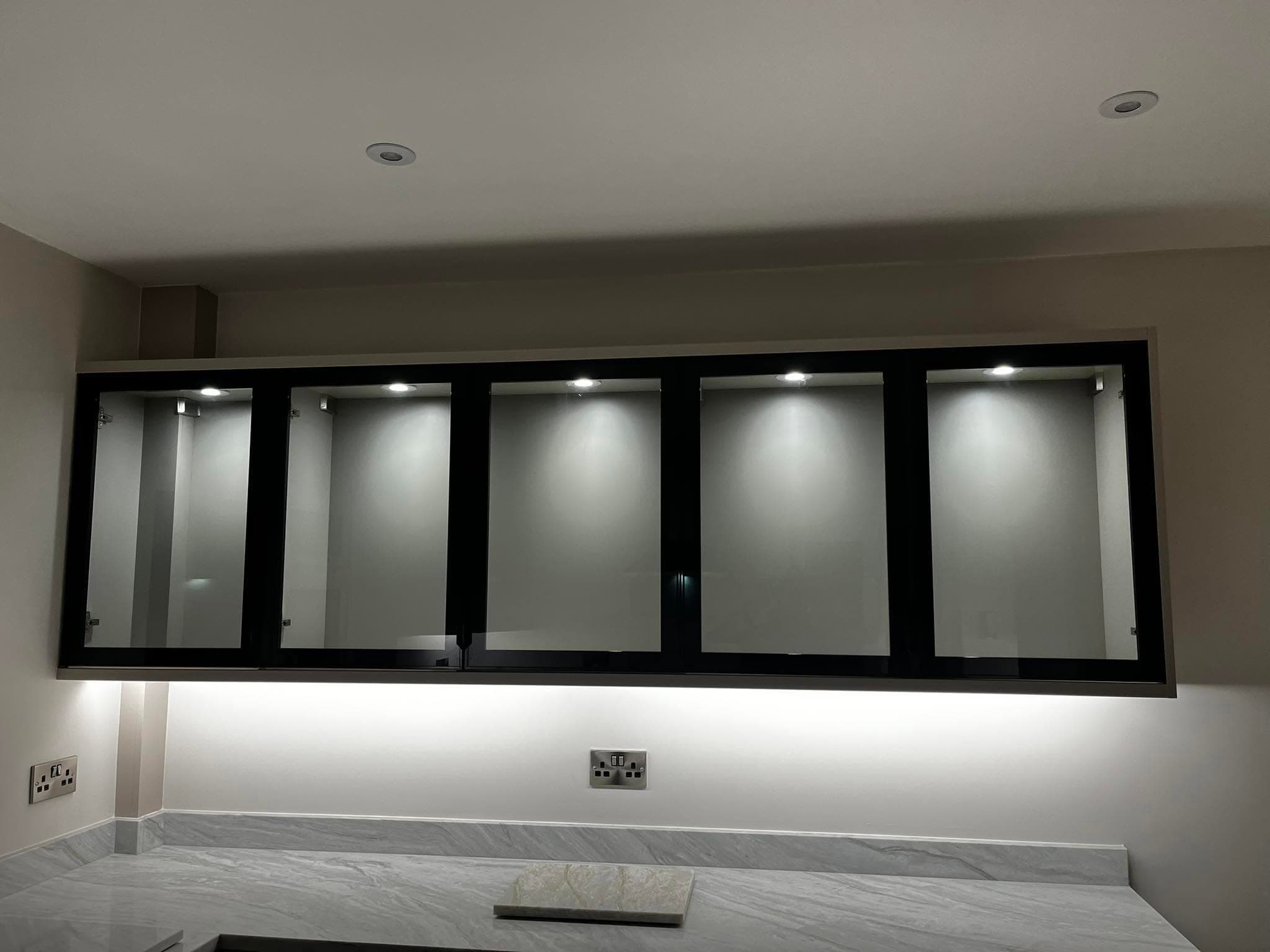 Kitchen with black-framed glass wall units lit by internal downlights and under-unit LED strip