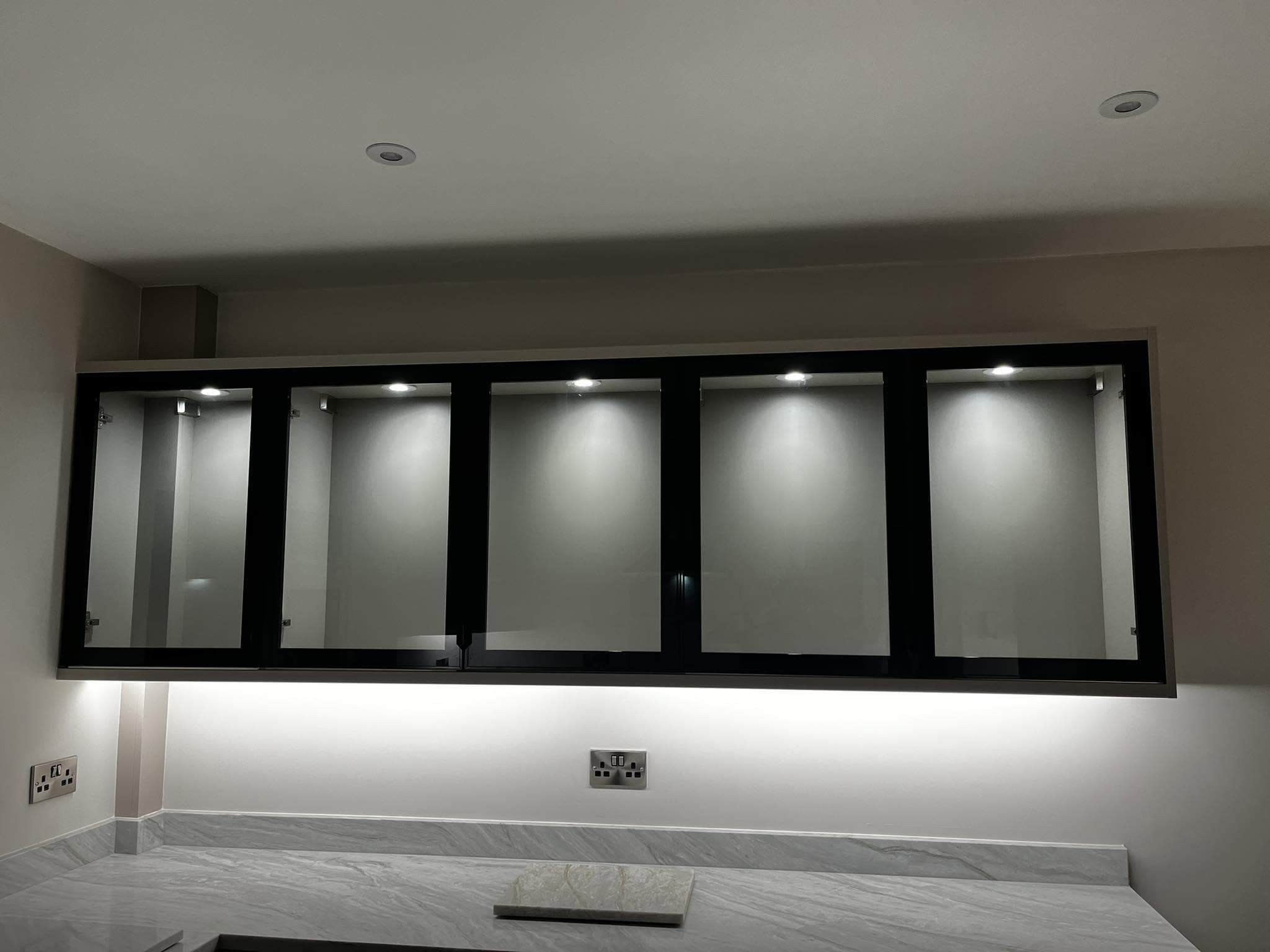 Kitchen with black-framed glass wall units lit by internal downlights and under-unit LED strip