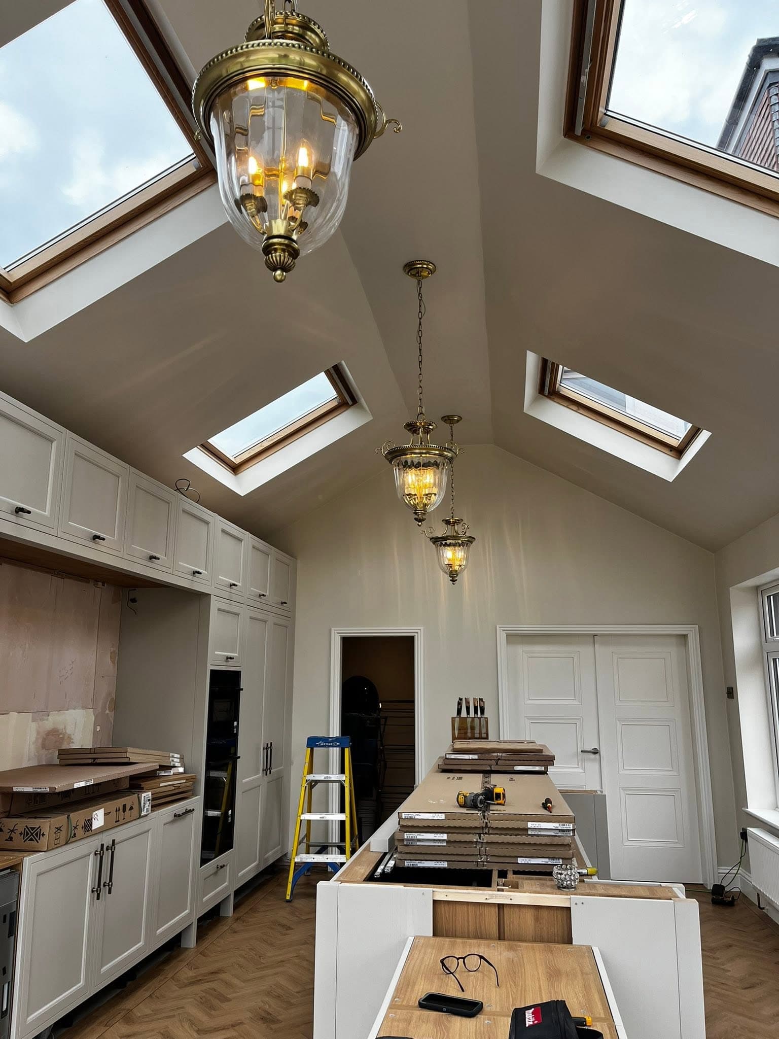 Brass lantern pendants being installed on a vaulted orangery ceiling with skylights