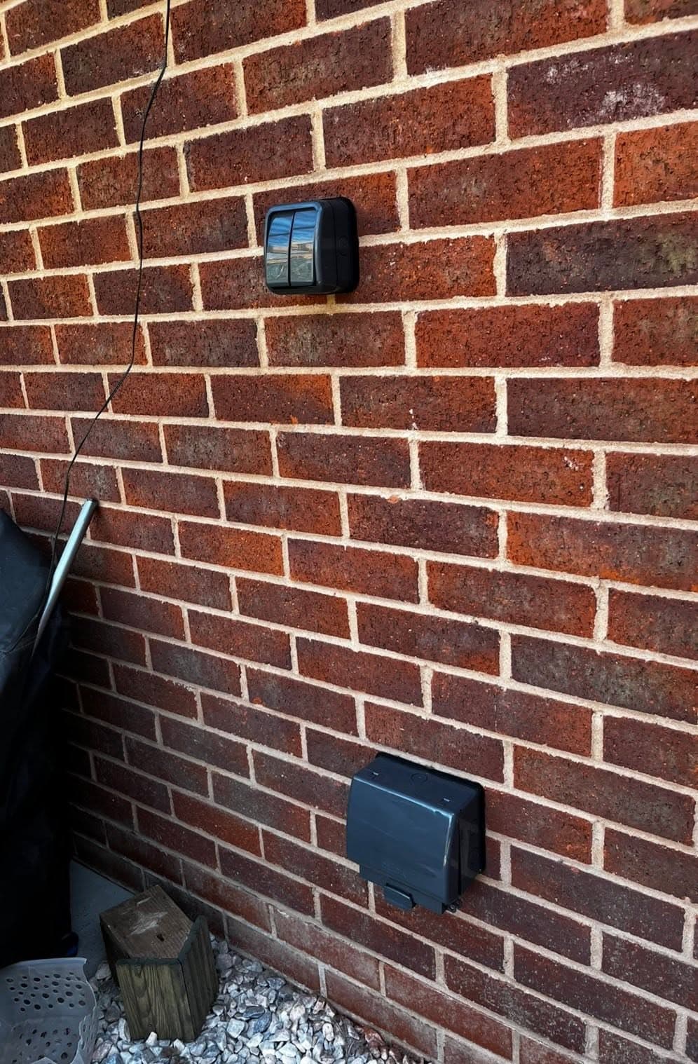 Weatherproof outdoor socket and a PIR security light fitted to a brick exterior wall