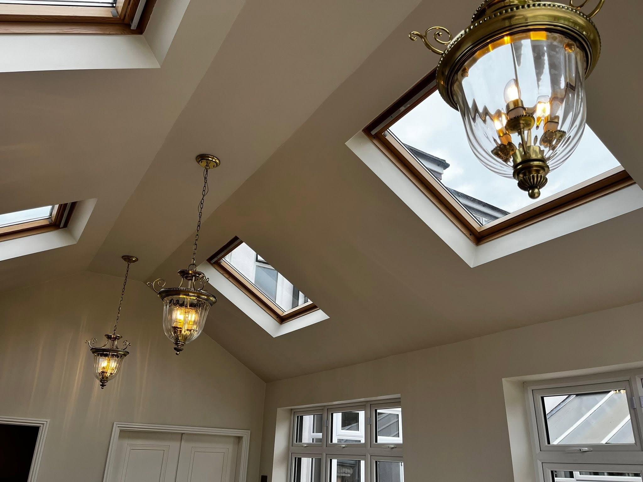 Finished brass lantern pendant lights hanging from a vaulted ceiling between skylights