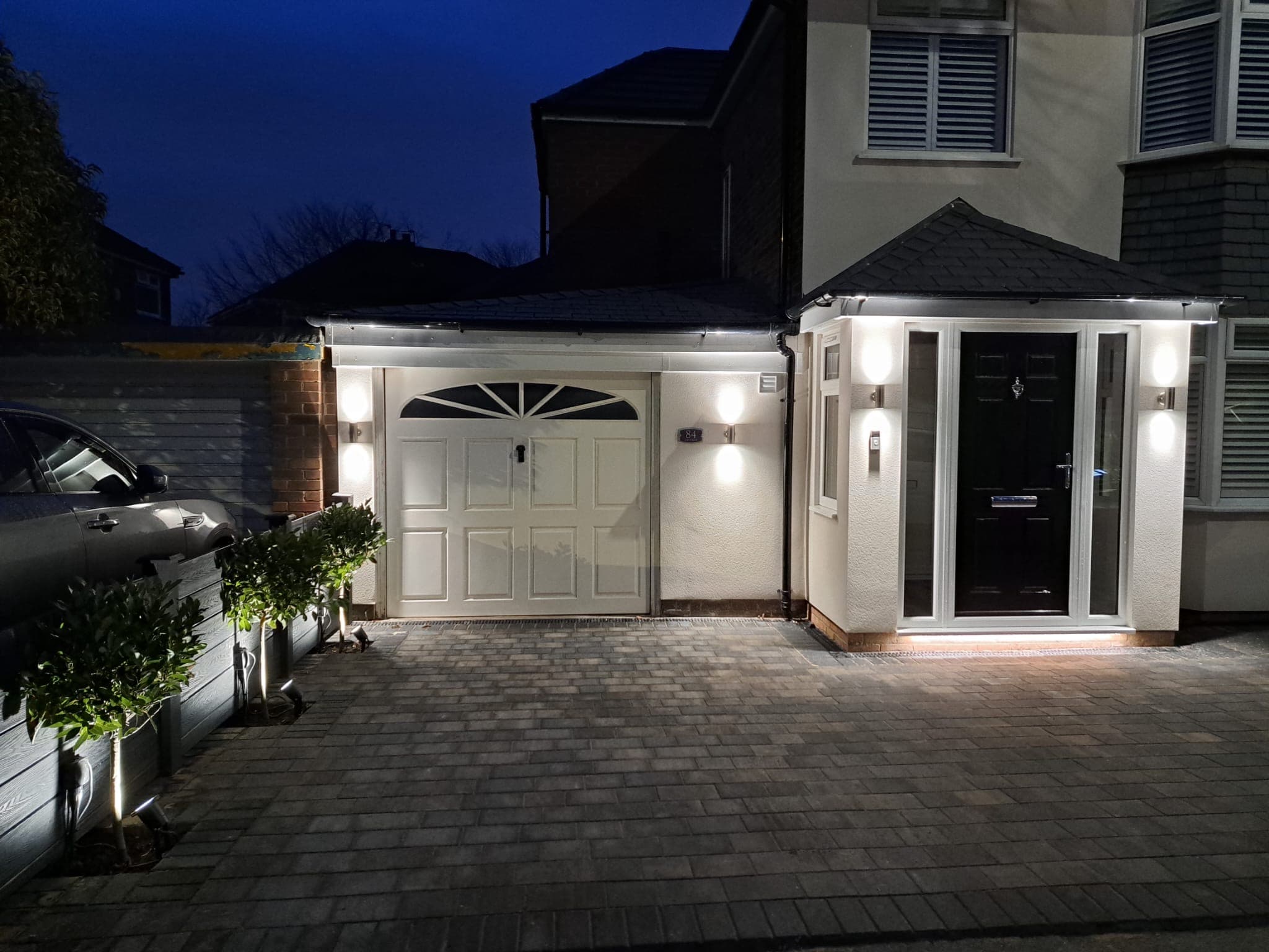 Driveway and porch lit at night with up and down wall lights either side of the garage and front door