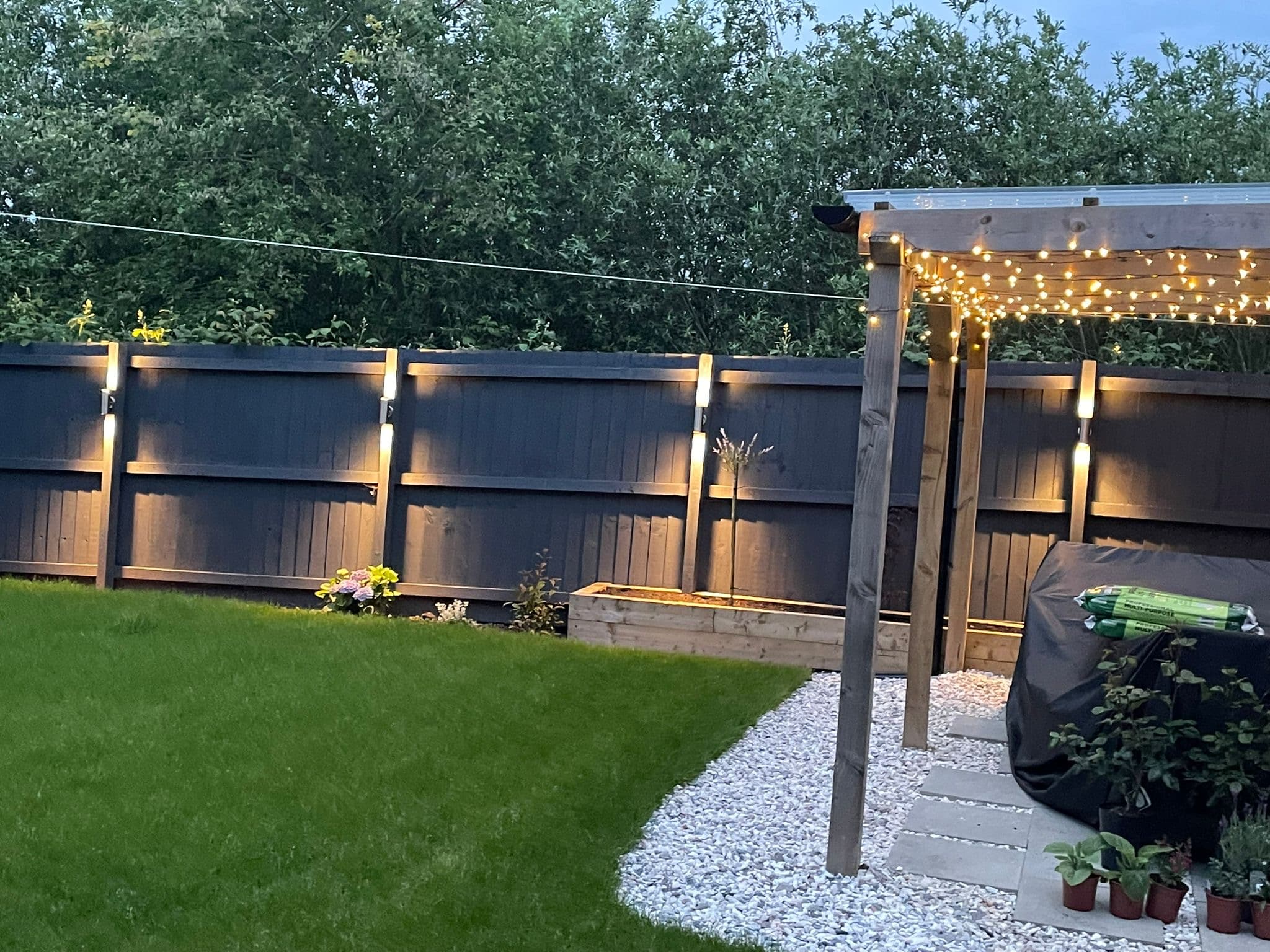 Landscaped garden at dusk with fence downlights and pergola festoon lighting, all cables hidden